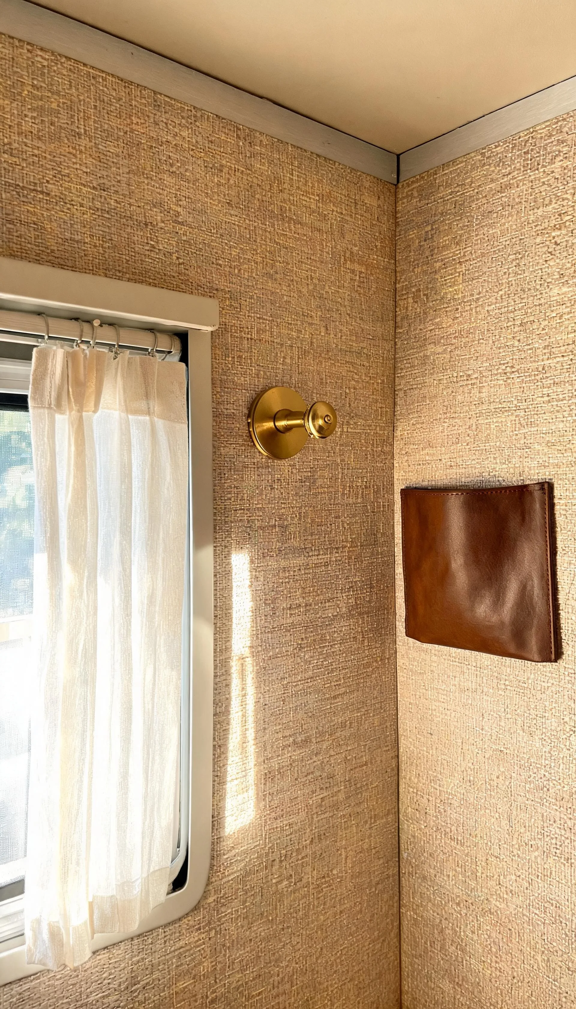 Camper wall in woven grasscloth-look peel-and-stick wallpaper with a linen curtain and small brass sconce