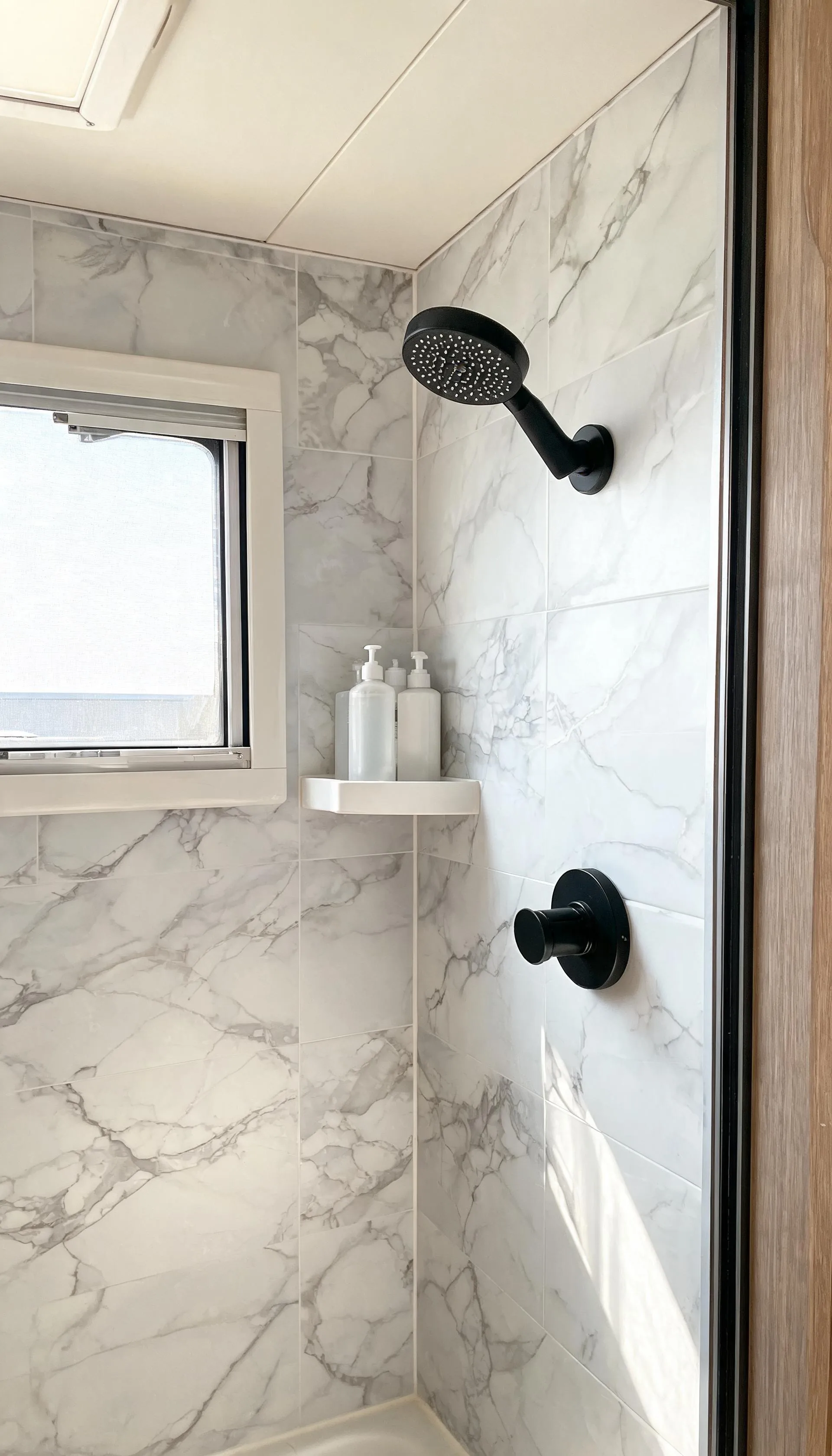Camper shower wall with waterproof marble-look vinyl peel-and-stick wallpaper and a small corner shelf