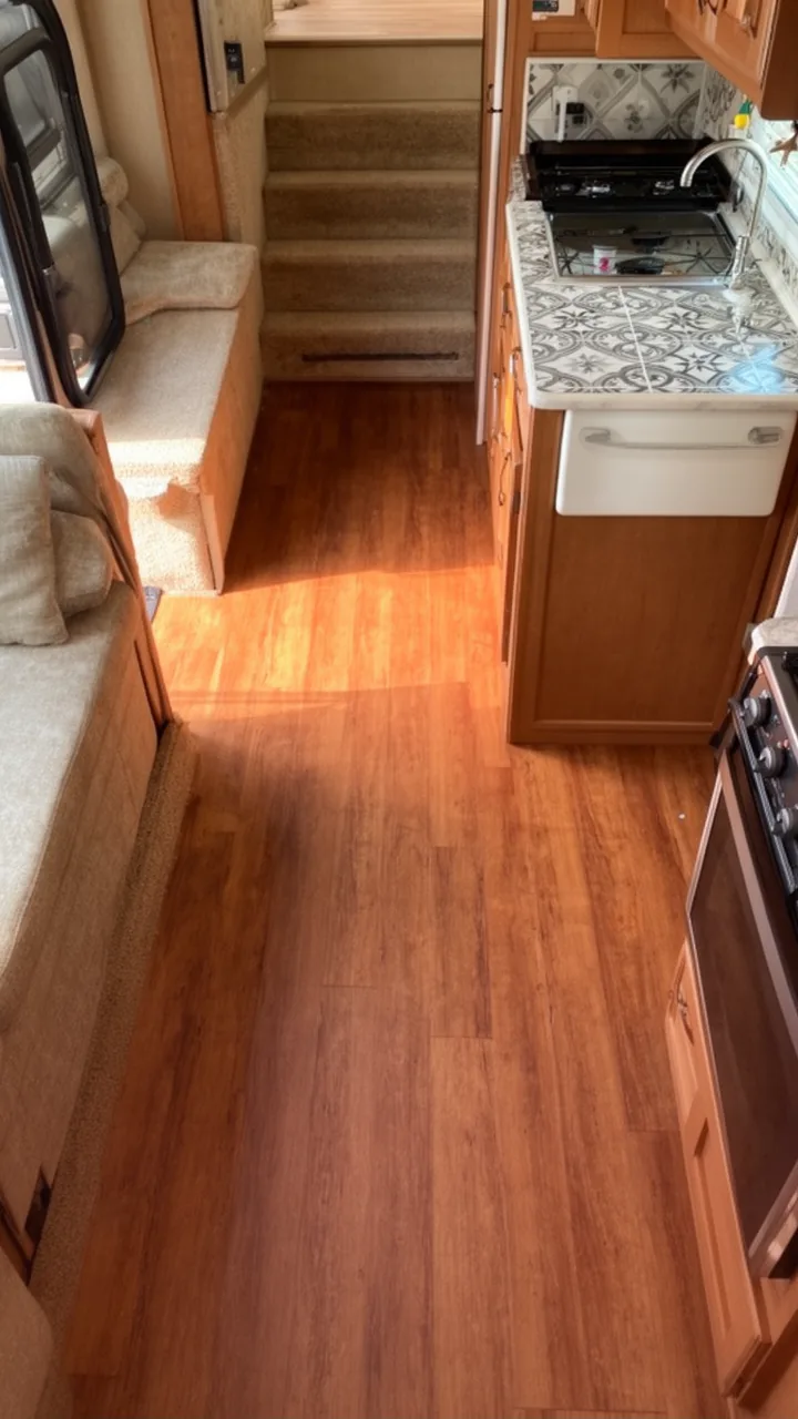 Two-tone camper floor with warm wood living area and patterned tile kitchen zone