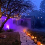 Outdoor Halloween lighting ideas: front yard at dusk with warm string lights in a bare tree, purple uplight on the house and glowing jack-o-lanterns lining the stone path in low fog